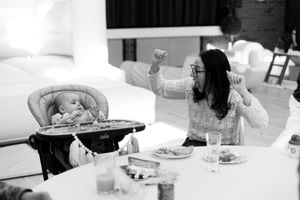 Black and white photo of a baby in a high chair at a table while a woman celebrates with raised fists.