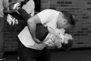 A man lovingly kisses a young child while lifting them up in a playful embrace outdoors.