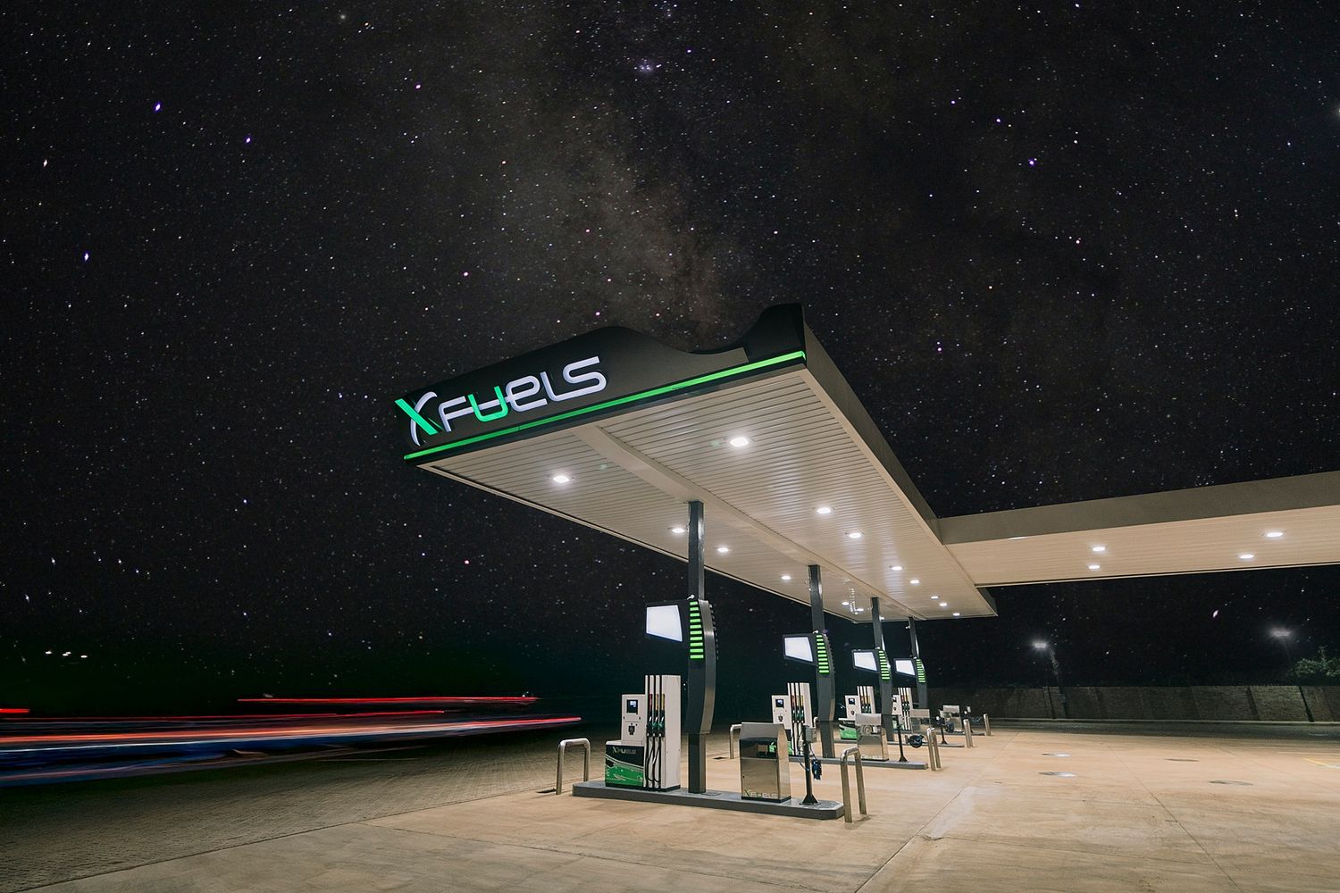 X Fuels gas station glowing under a stunning starry night sky with the Milky Way visible above.