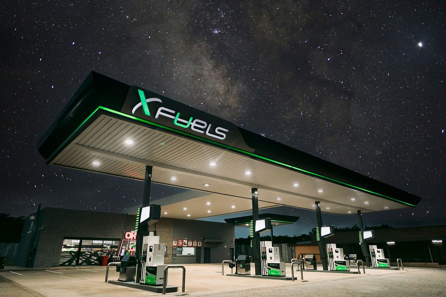 XFuels gas station illuminated at night under a stunning Milky Way sky with green and white lighting.