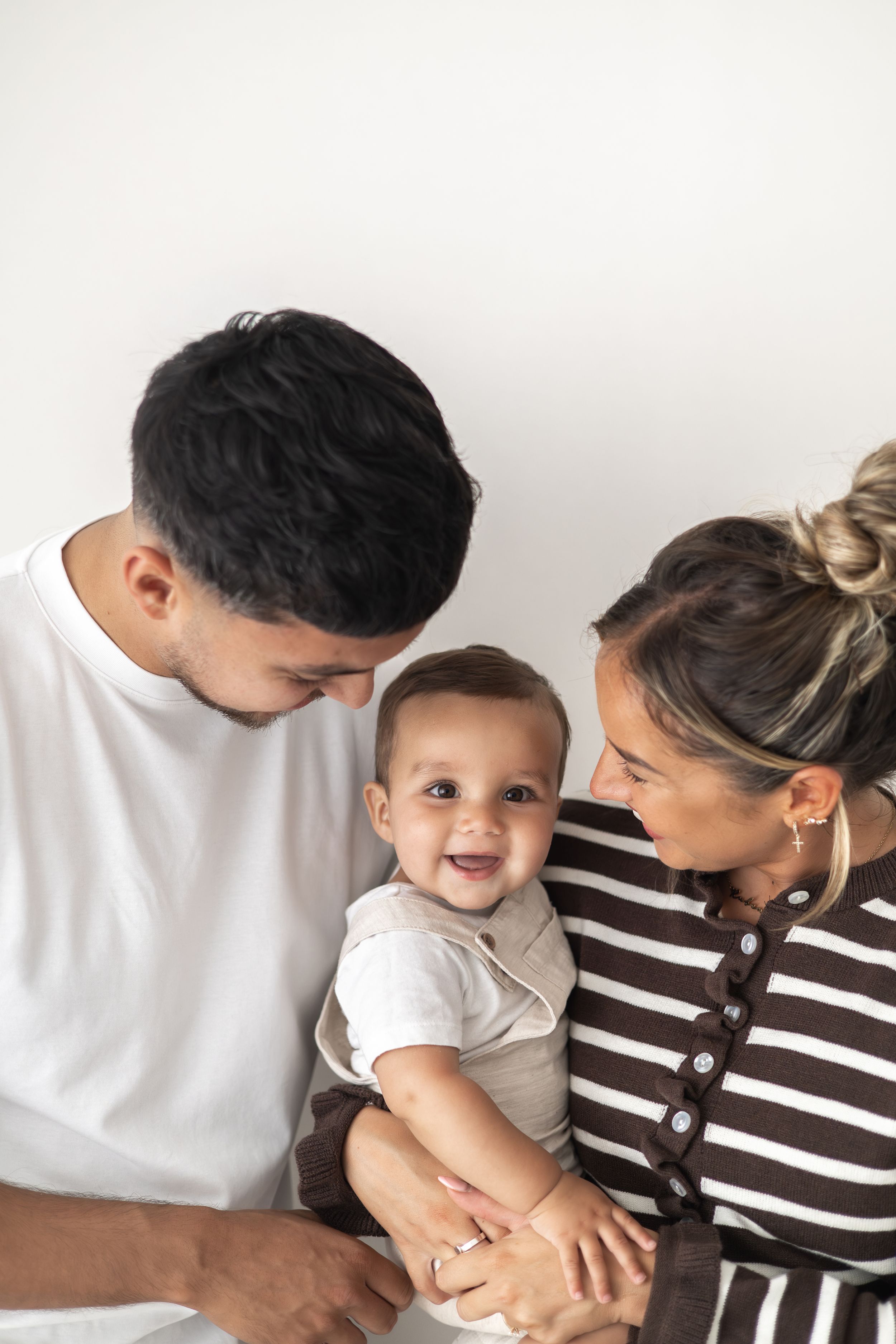 A family with a smiling baby being held by parents against a white background natural 1st birthday photoshoot Nottingham