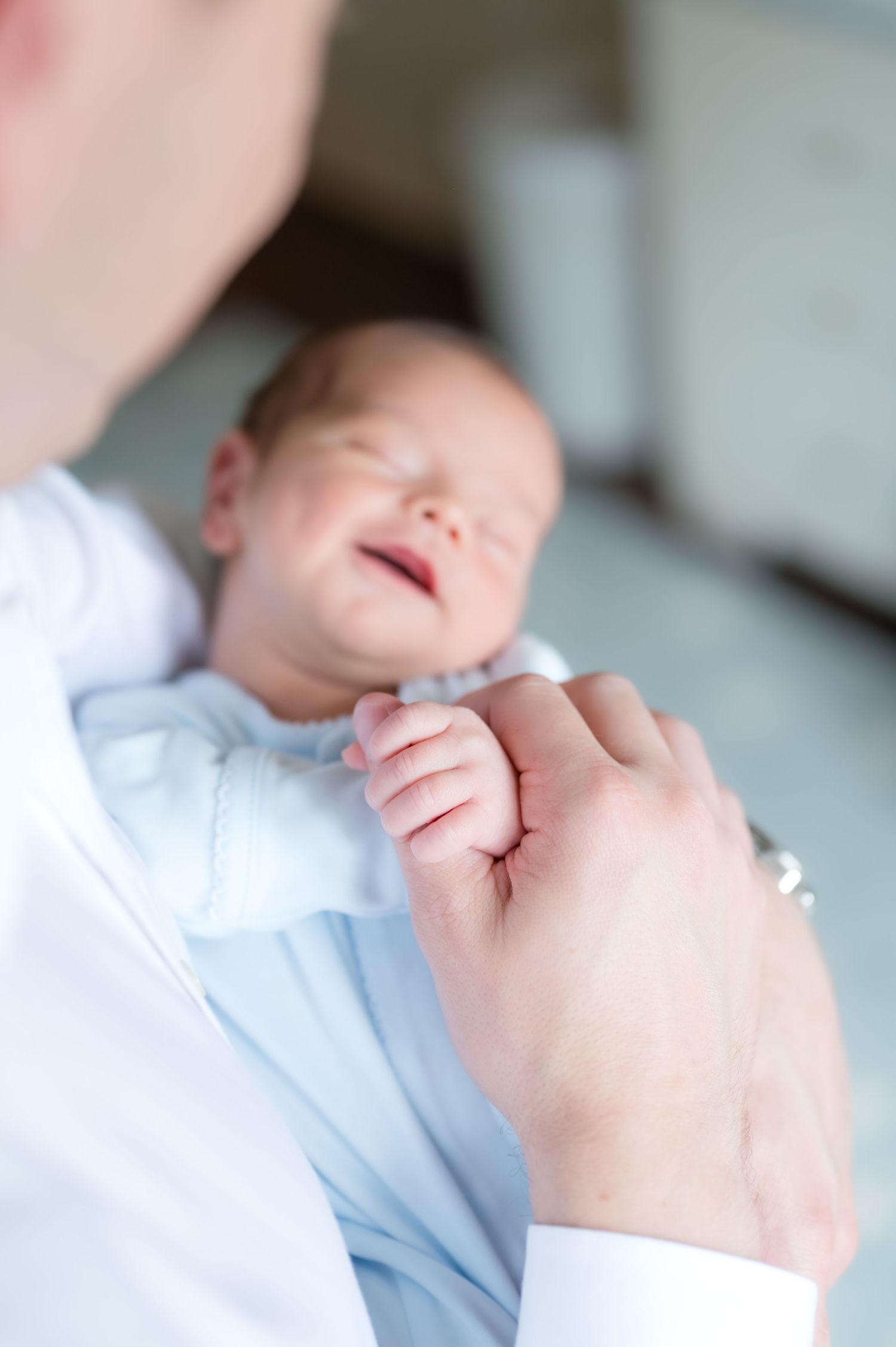 Father holding his newborn baby who is holding his finger and smiling.