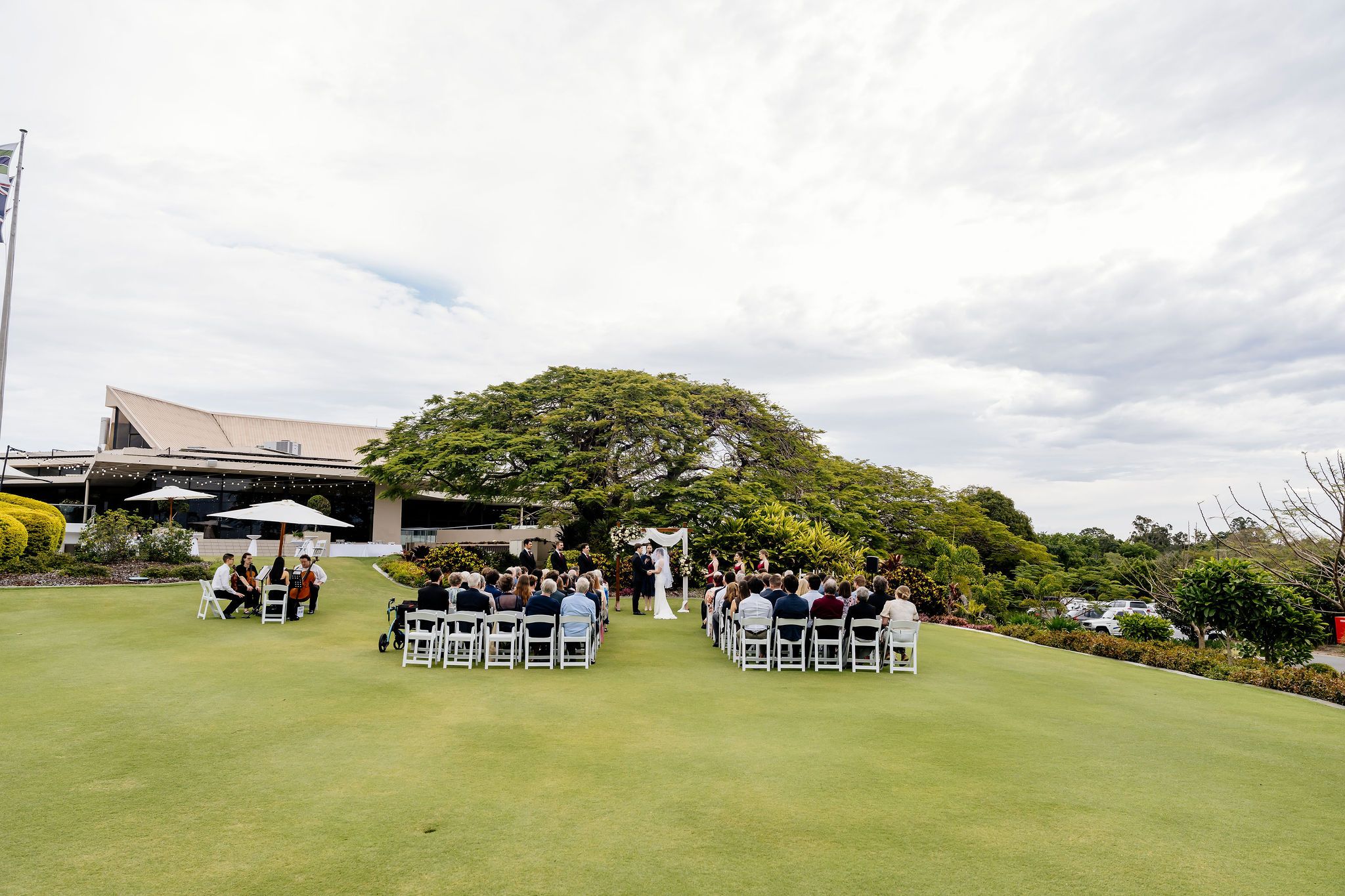 Outdoor wedding ceremony on lush green golf course with white chairs, floral arch, and elegant clubhouse backdrop in Brisbane, Queensland