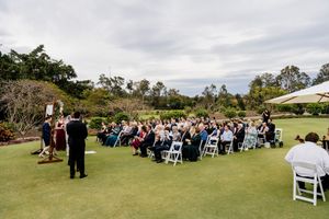 Outdoor wedding ceremony on lush green lawn with guests seated in white chairs under cloudy skies in Brisbane, Queensland