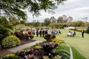 Outdoor wedding ceremony on a manicured lawn surrounded by lush tropical gardens under a cloudy sky Indooroopilly Golf Club Brisbane