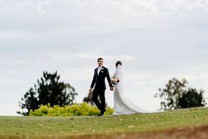 Bride and groom walking hand in hand across a green lawn on their wedding day under a cloudy sky Indooroopilly Golf Club Brisbane Queensland