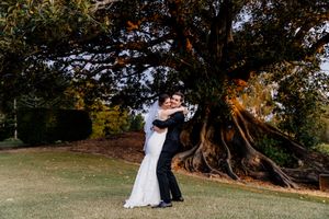 Bride and groom embracing on green lawn beside a large ancient tree on their wedding day Indooroopilly Golf Club Brisbane Queensland