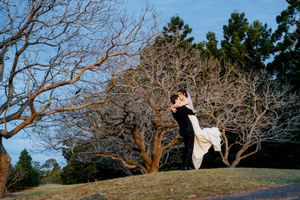 Bride and groom embrace on a grassy hill surrounded by bare winter trees under a clear blue sky at Indooroopilly Golf Club Brisbane