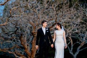 A bride and groom hold hands and smile at each other outdoors, with dramatic bare trees in the background at dusk at Indooroopilly Golf Club