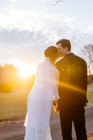 A bride and groom share a romantic kiss at sunset, bathed in golden light with a soft blue sky backdrop Indooroopilly Golf Club Brisbane QLD