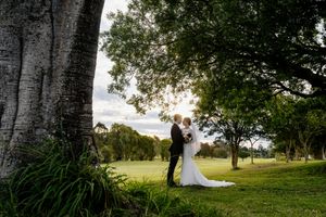 Bride and groom share romantic moment under large trees on lush green golf course at golden hour Indooroopilly Golf Club Brisbane QLD