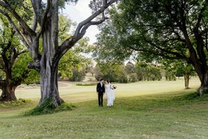 Wedding couple standing beneath large trees on a lush green golf course lawn on their wedding day Indooroopilly Golf Club Brisbane QLD