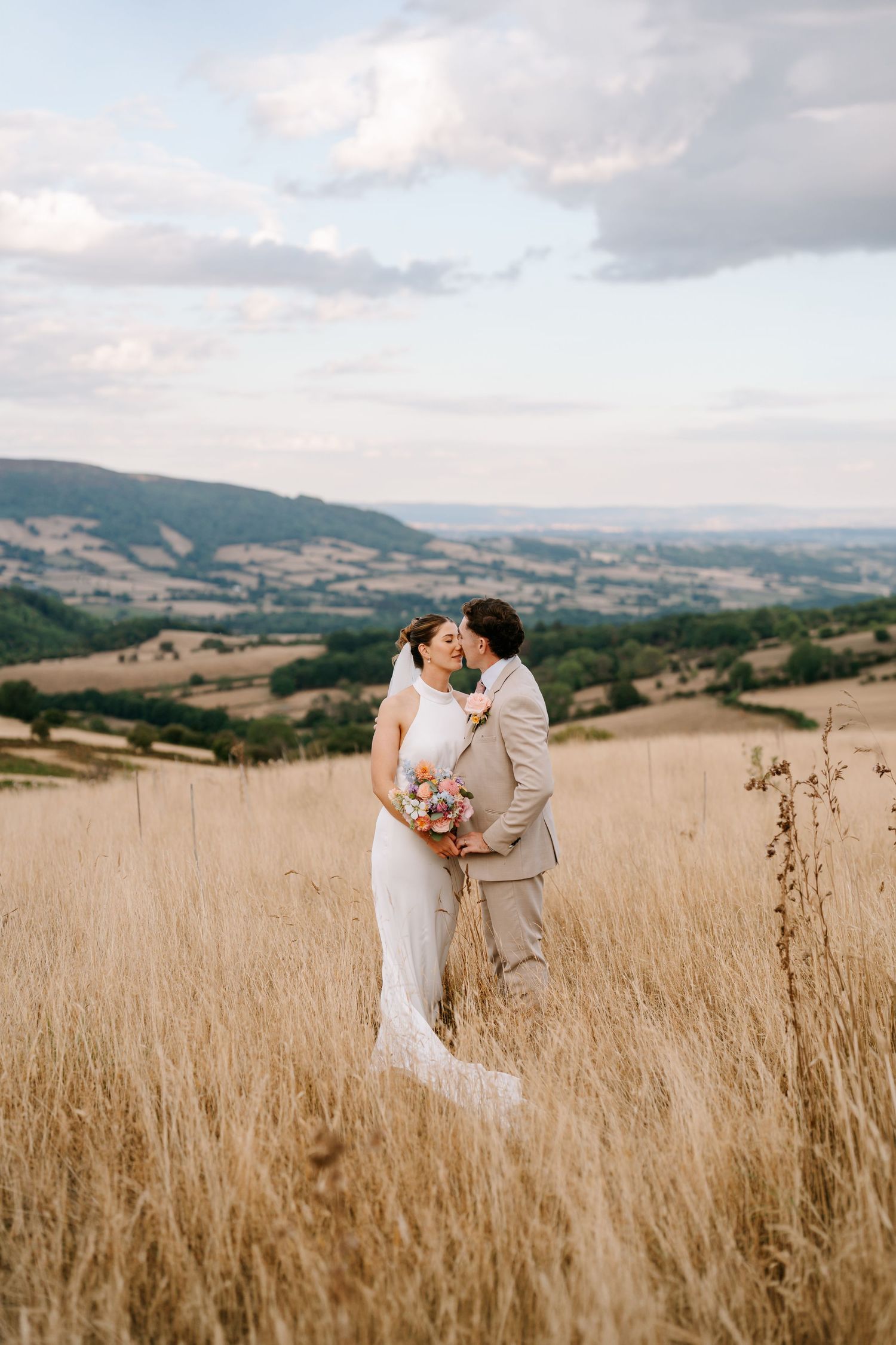 A wedding couple walks hand in hand down a path leading to a grand Gothic-style castle in the background.