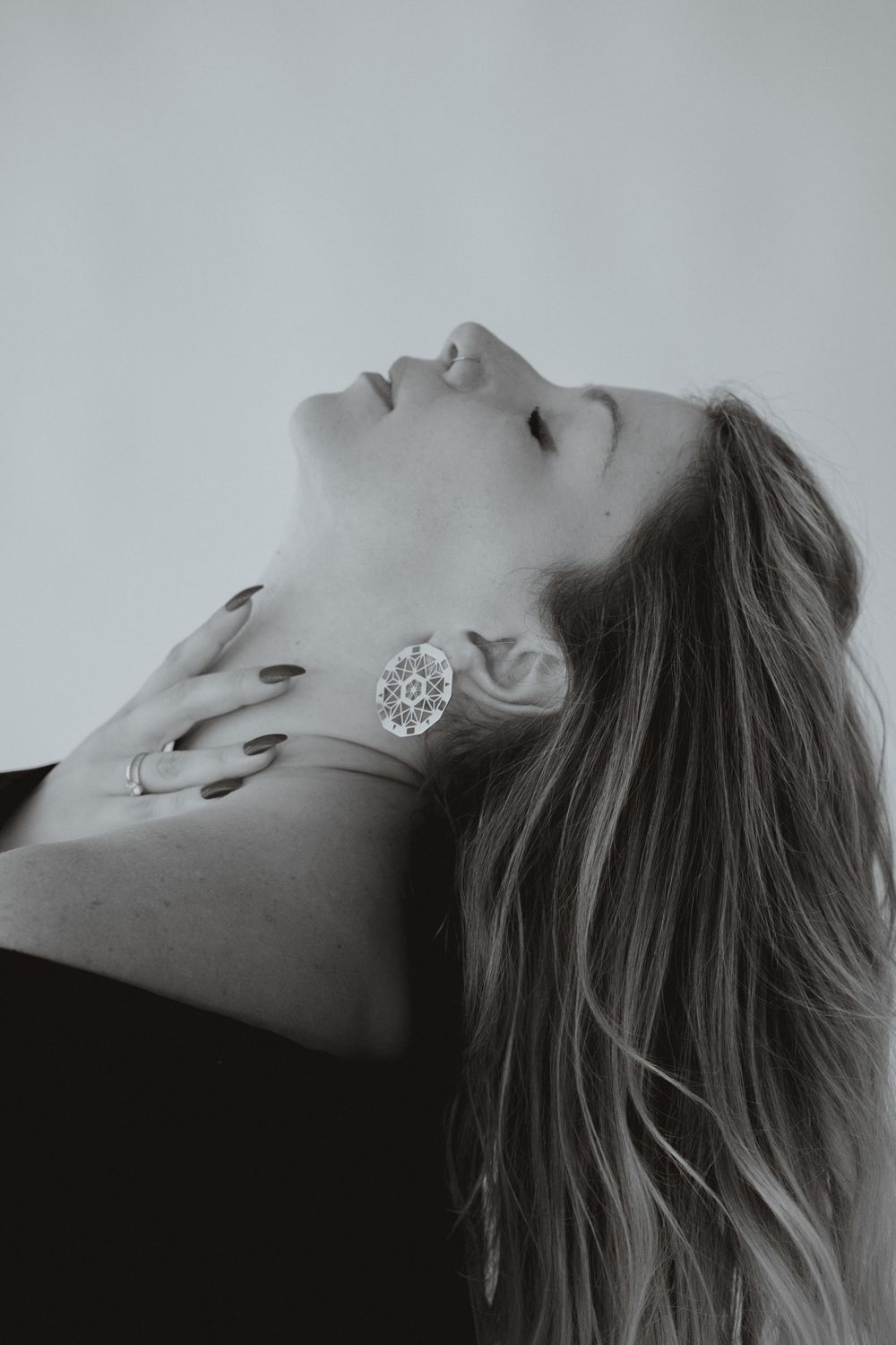 Black and white photo of a woman with long hair, head tilted back, wearing a decorative oval ring and dark nail polish.