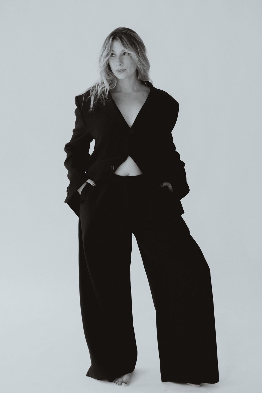 Woman in black wide-leg pantsuit with cropped blazer poses confidently in black and white fashion photo.