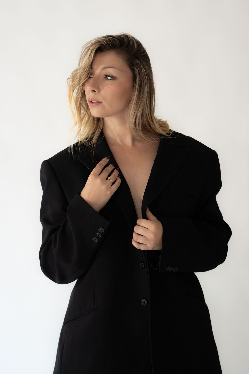Woman in oversized black blazer coat posing against white background with blonde hair.