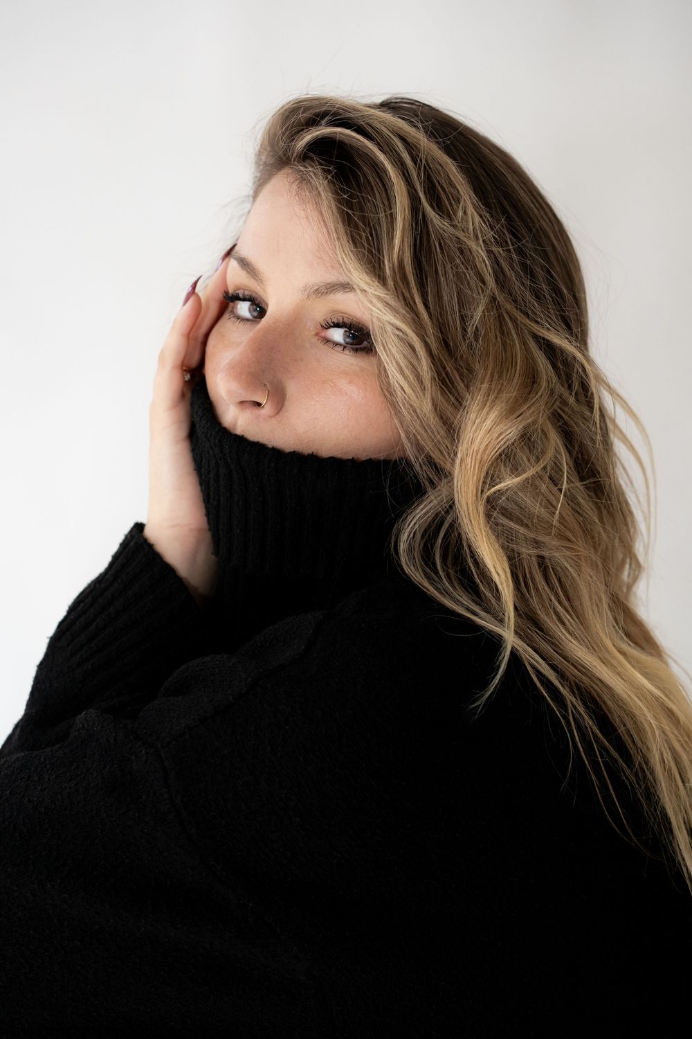 Woman in black turtleneck sweater with wavy blonde hair posing against white background.