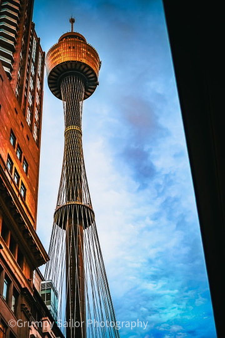 Sydney Tower Eye soaring against blue sky viewed from street level.