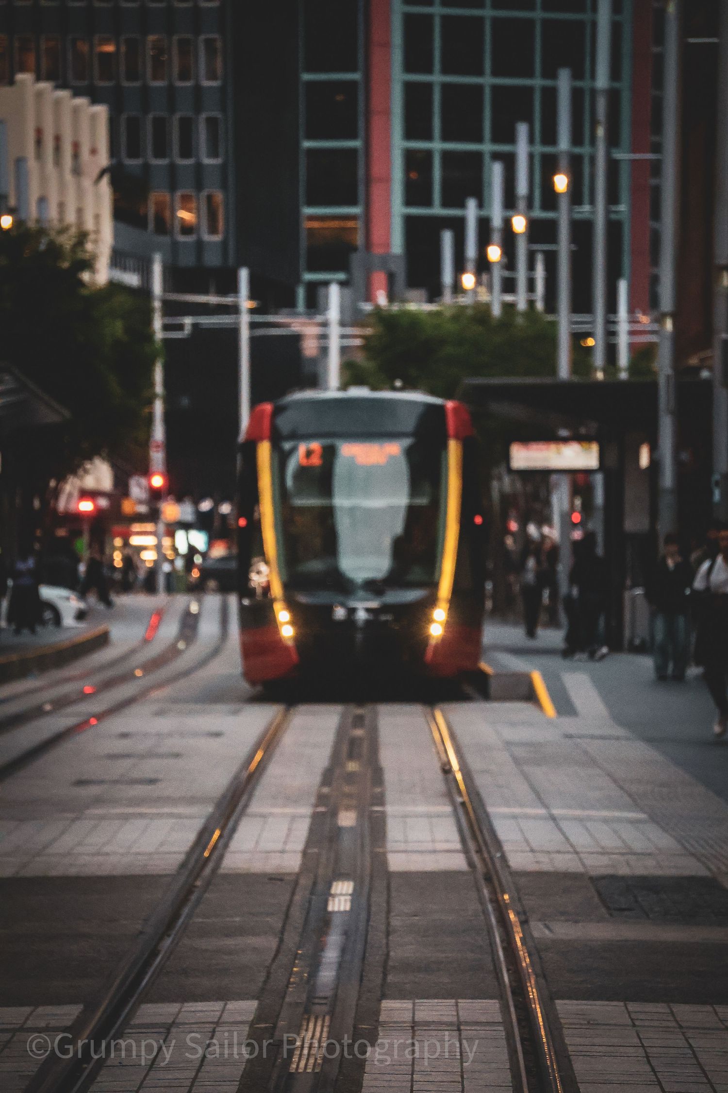 Red light rail tram approaching on city tracks at dusk.