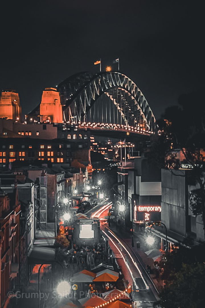 Sydney Harbour Bridge illuminated at night with city streets below.