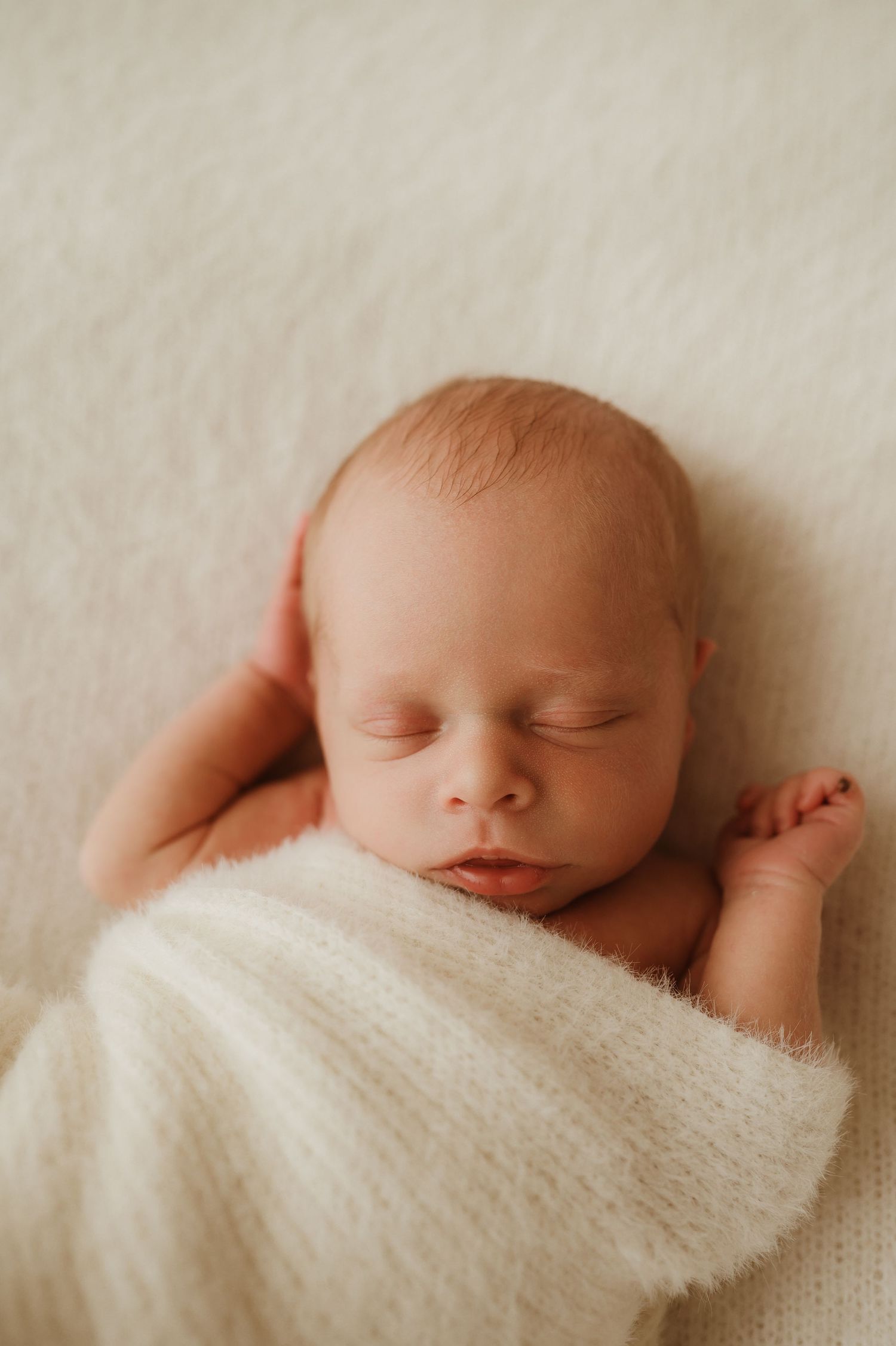 Infant wearing a cozy cream-colored ribbed sweater onesie with wooden buttons while resting on beige textiles.