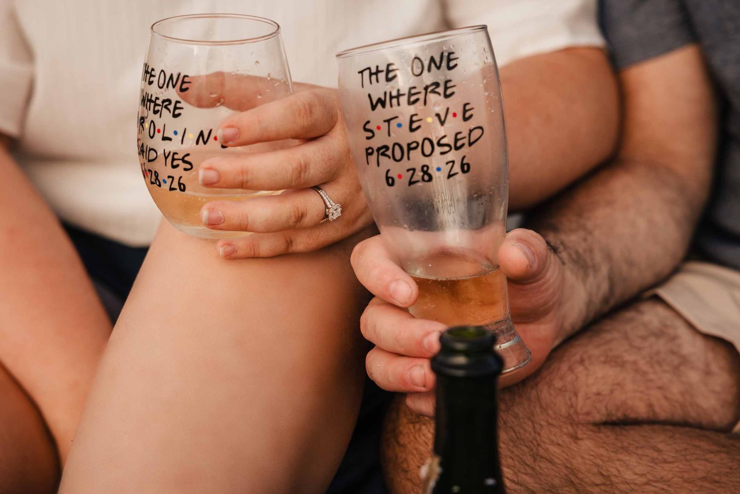 Close-up of personalized champagne glasses reading 'the one where Caroline said yes' and 'the one where Steve proposed.'