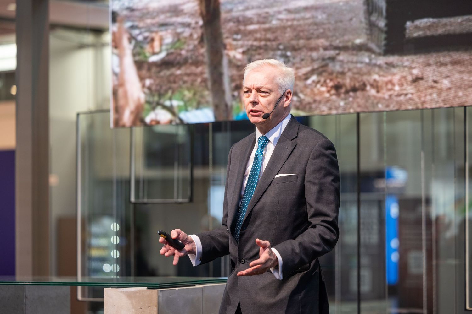 Senior executive delivers a keynote speech at an indoor trade show exhibition stage.