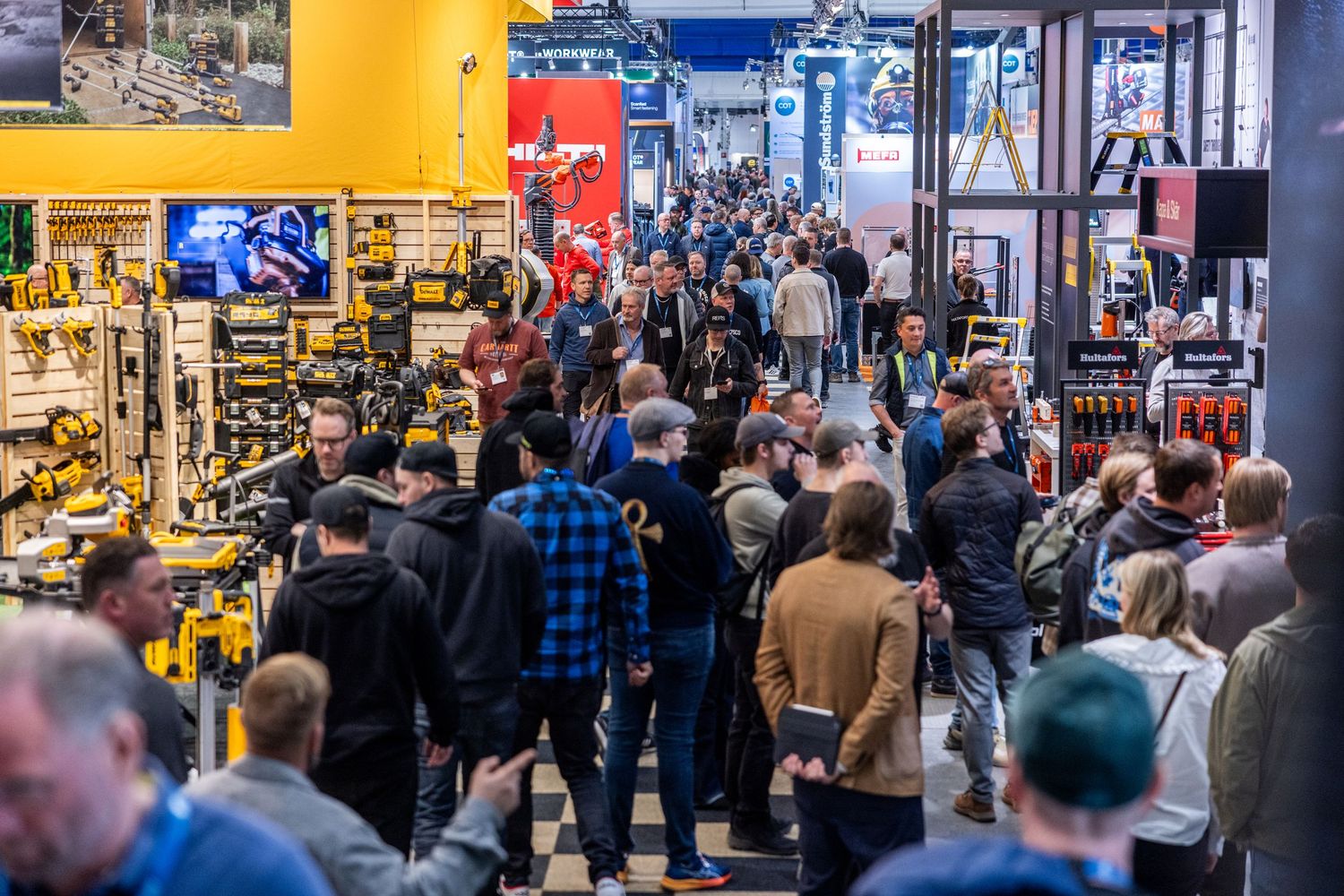 Crowded trade show exhibition hall with visitors browsing construction and tool displays.