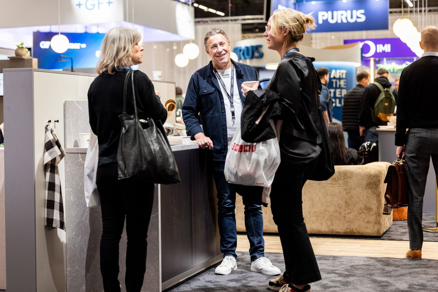 Three professionals networking and conversing at a trade show exhibition booth.