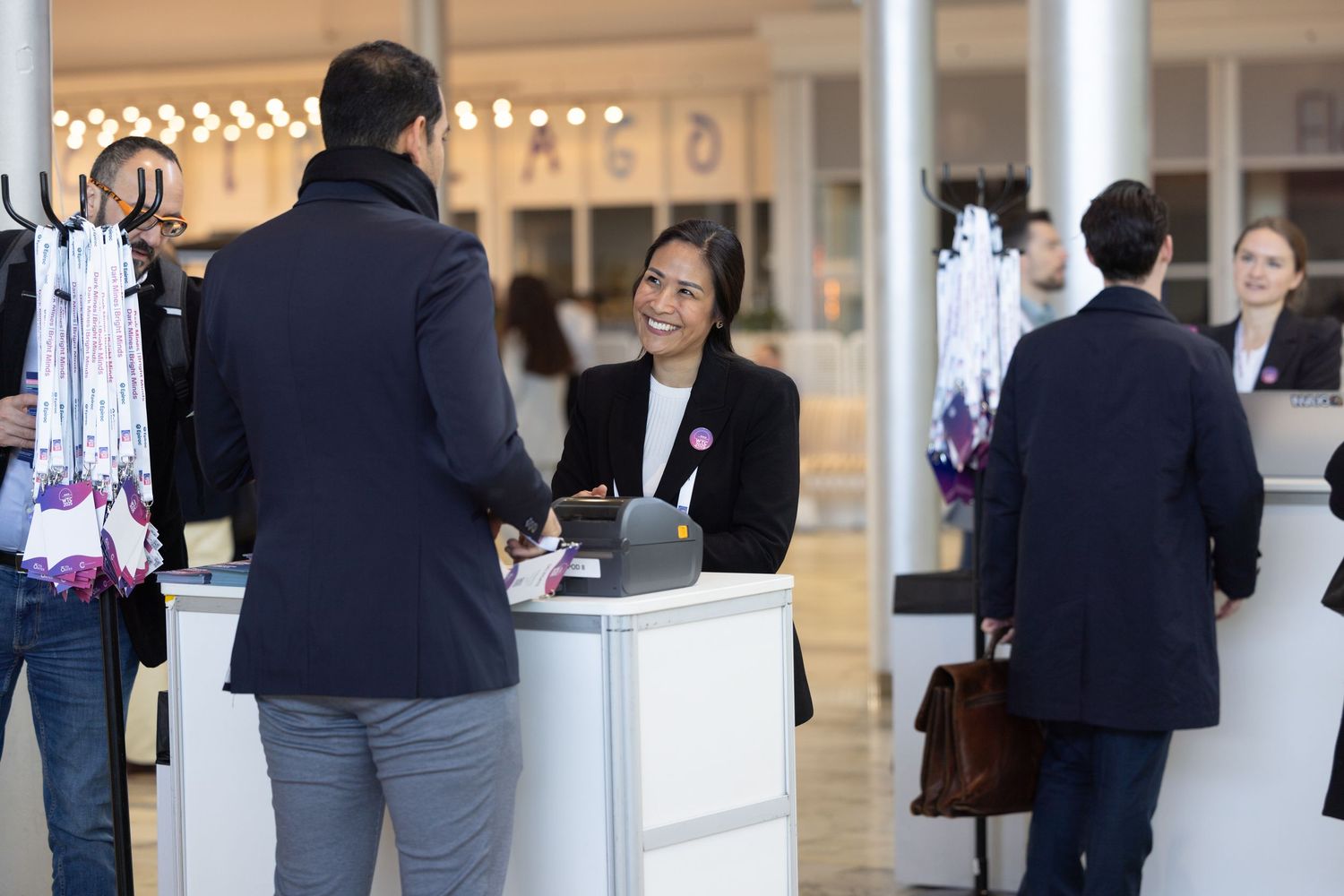 A smiling female receptionist assists a guest at a registration desk in a bright event venue.