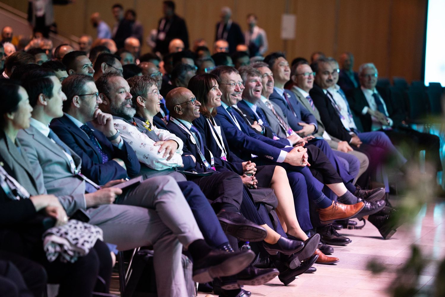 A diverse audience of professionals seated in rows attentively watching a presentation at a conference.