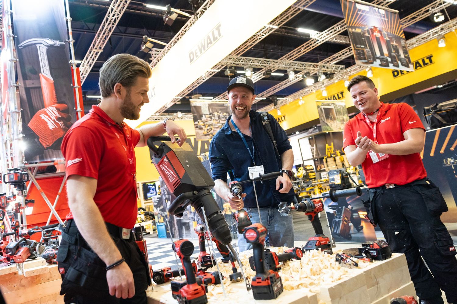 Two staff members in red uniforms demonstrate power tools to a customer at a trade show exhibition booth.