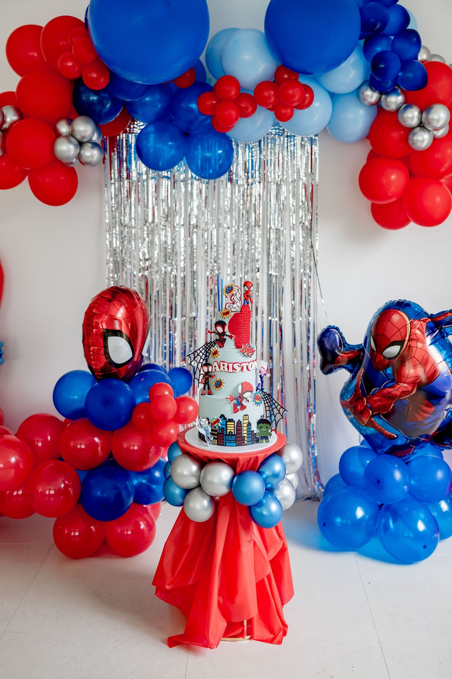 Spiderman themed birthday party setup with balloon arch in red, blue and silver with decorated cake.