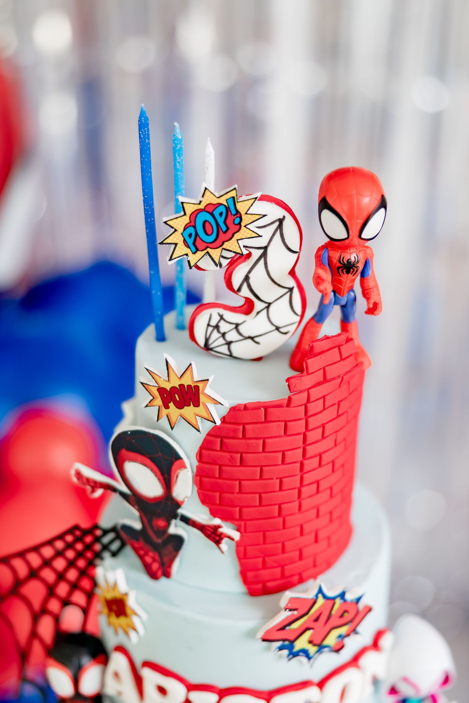 Close-up of Spiderman birthday cake top tier with number 3 candle and superhero figurines.