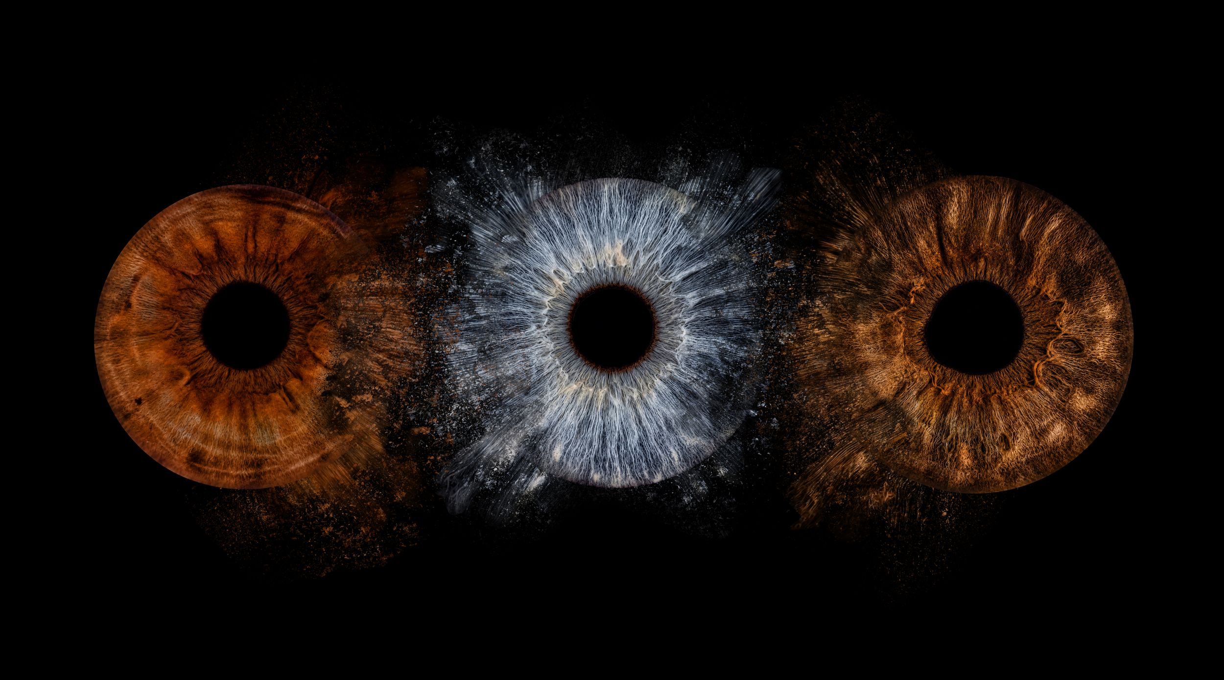 Three macro human eyes with brown, blue, and amber irises displayed side by side on a black background.
