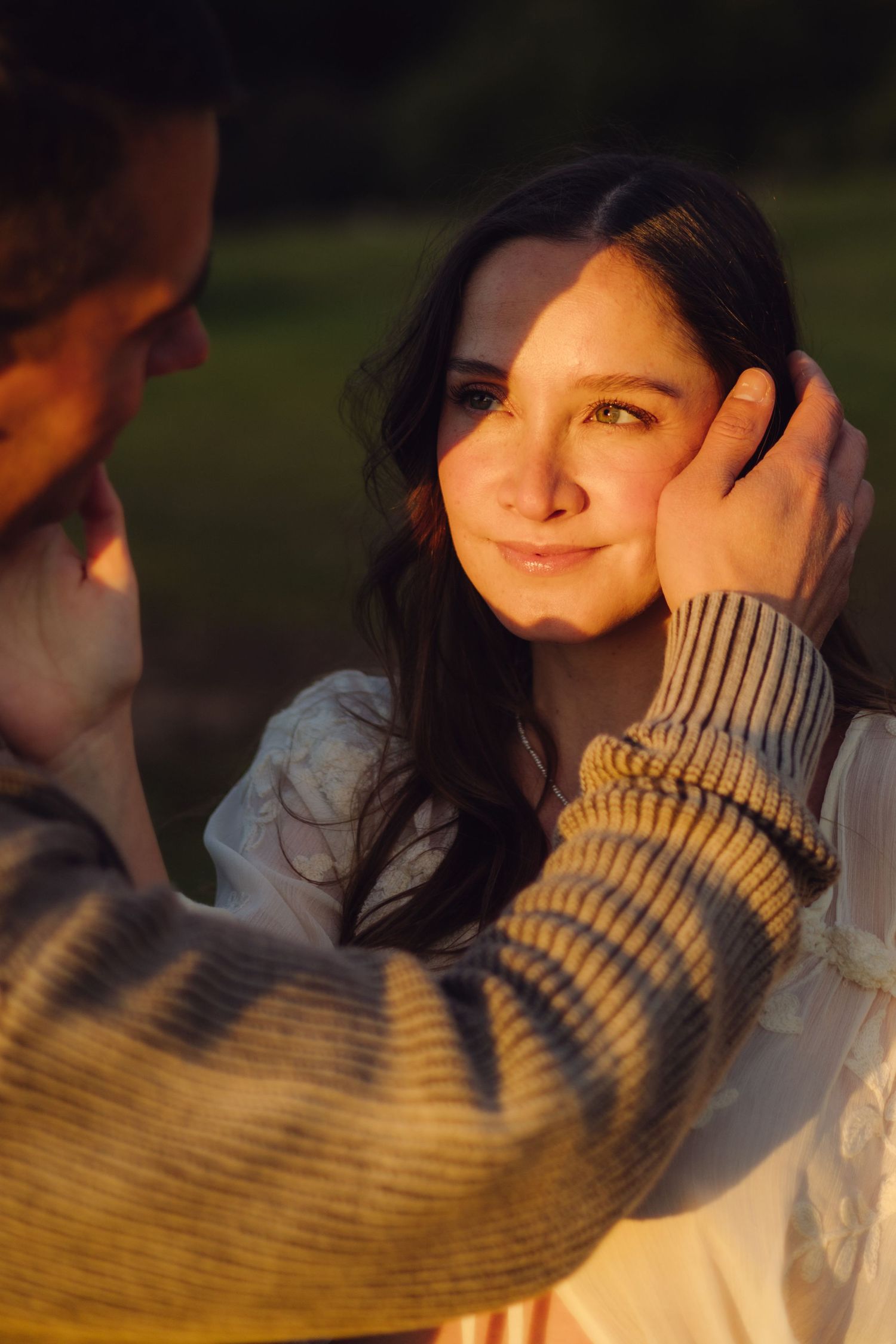 Man tenderly cupping pregnant woman's face in warm golden sunset light during outdoor maternity photoshoot.
