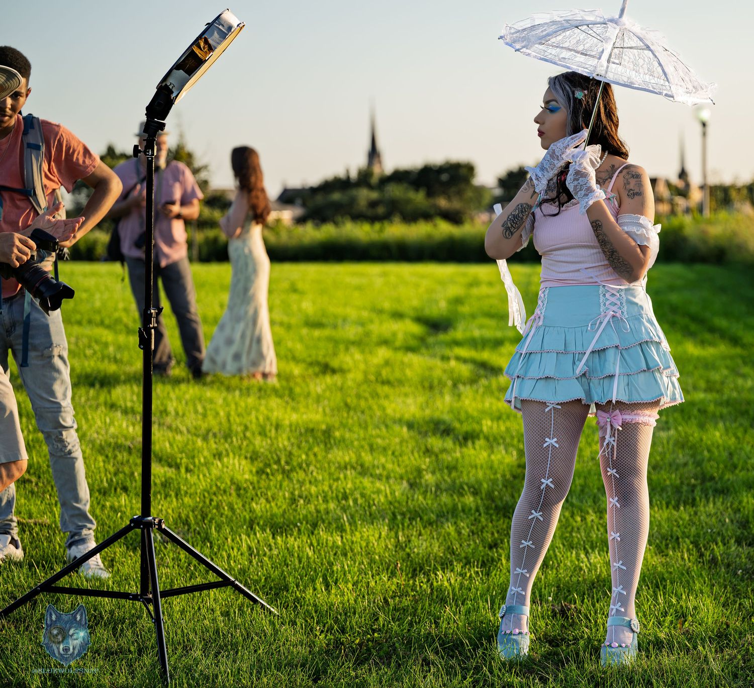 Woman in blue skirt holding white parasol poses outdoors on green grass during a professional photo shoot.
