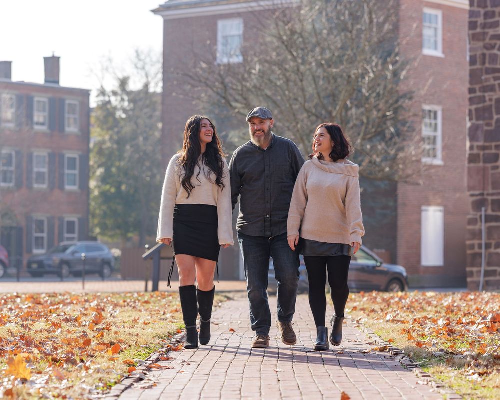 Three people walking together on a brick path surrounded by autumn leaves near a red brick university building.