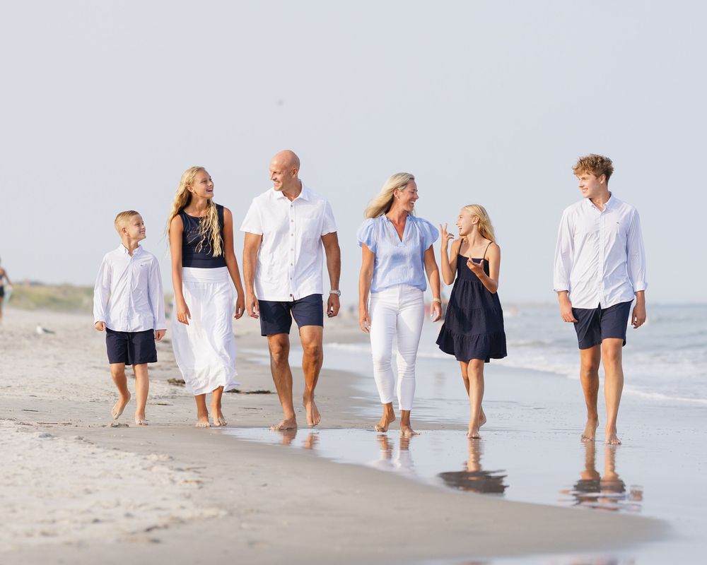 Family of six walking together on a sandy beach in white and navy outfits on a sunny day.