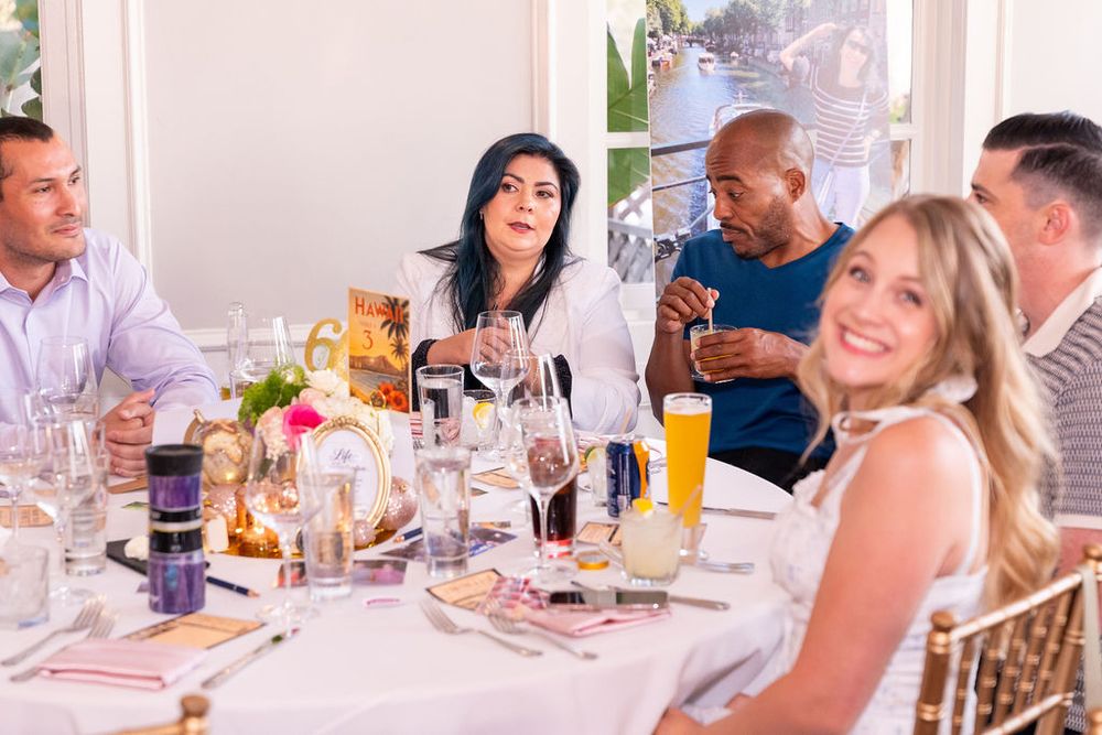 Group of friends enjoying a lively dinner party at an elegant white-tablecloth restaurant with drinks and floral centerpieces.