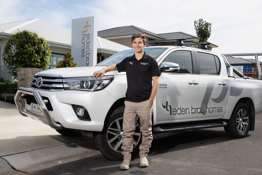 An Eden Brae Homes representative stands proudly beside a branded white Toyota HiLux ute outside a display home.