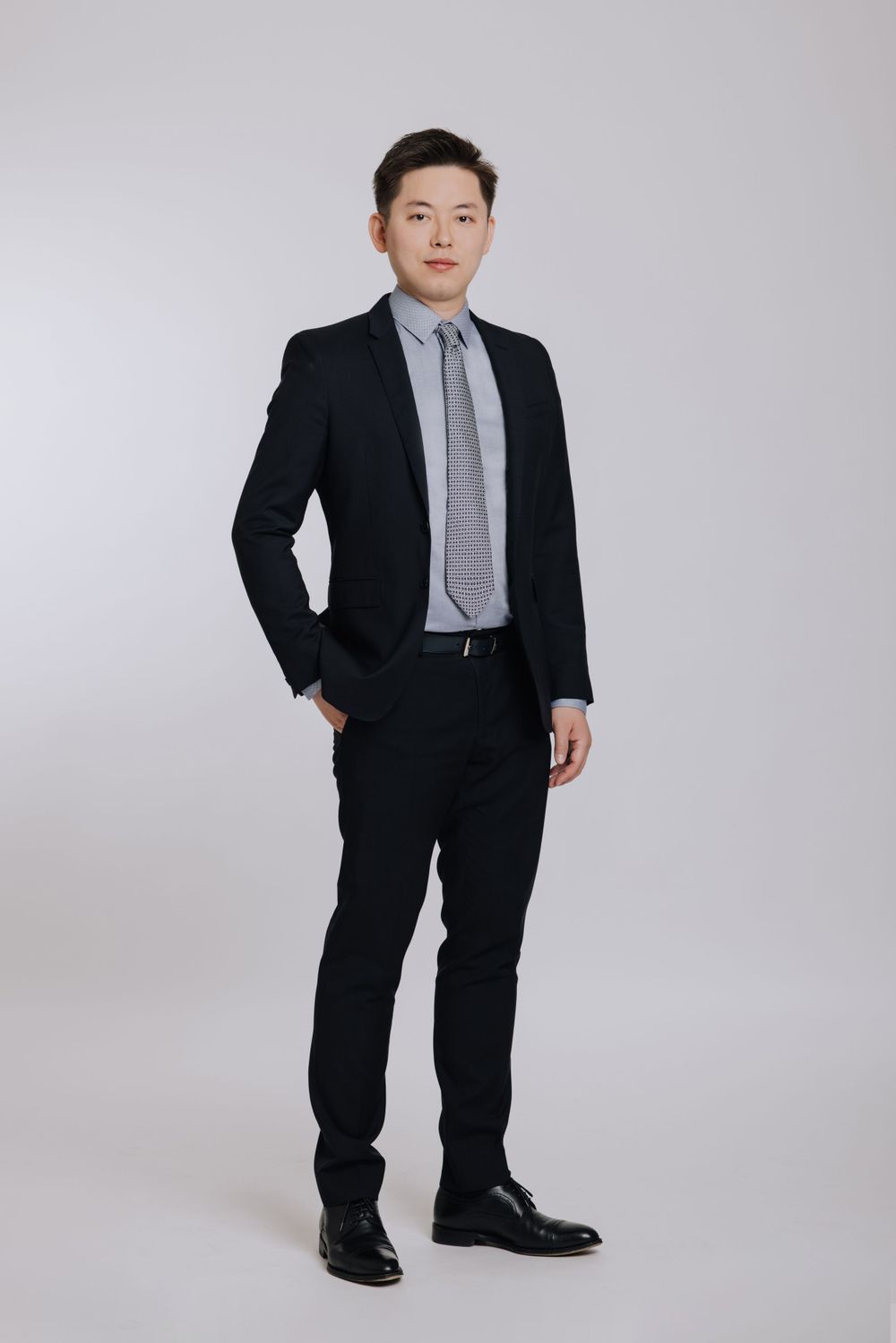 Young Asian businessman in black suit and striped tie posing for a full-length professional portrait.