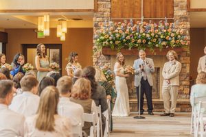 Wedding ceremony indoors with bride, groom, and officiant standing before floral fireplace mantel.