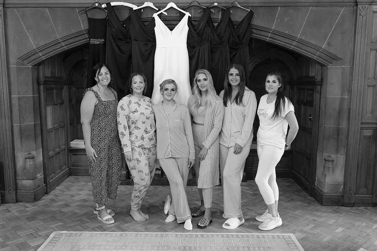 Bride and bridesmaids stand in front of the grand fireplace at Dalston Hall wedding venue