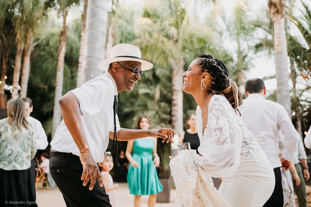 Couple dancing joyfully at an outdoor wedding reception surrounded by palm trees and guests.