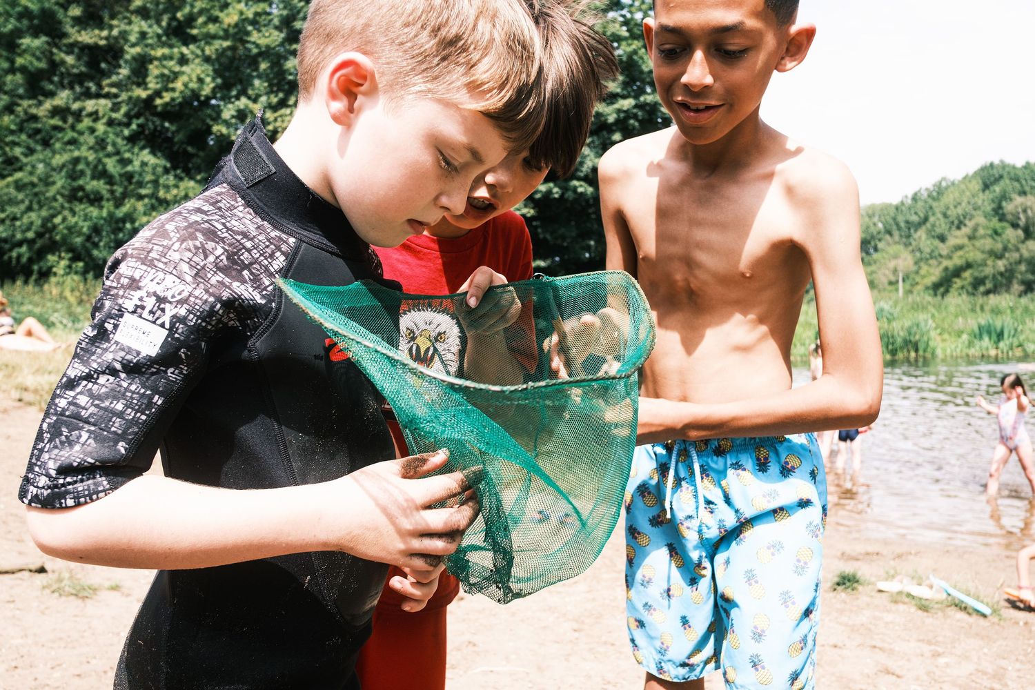 Suffolk Wildlife Trust: Two boys examining the contents of a fishing net by a lake on a sunny summer day outdoors. Photo by John Ferguson