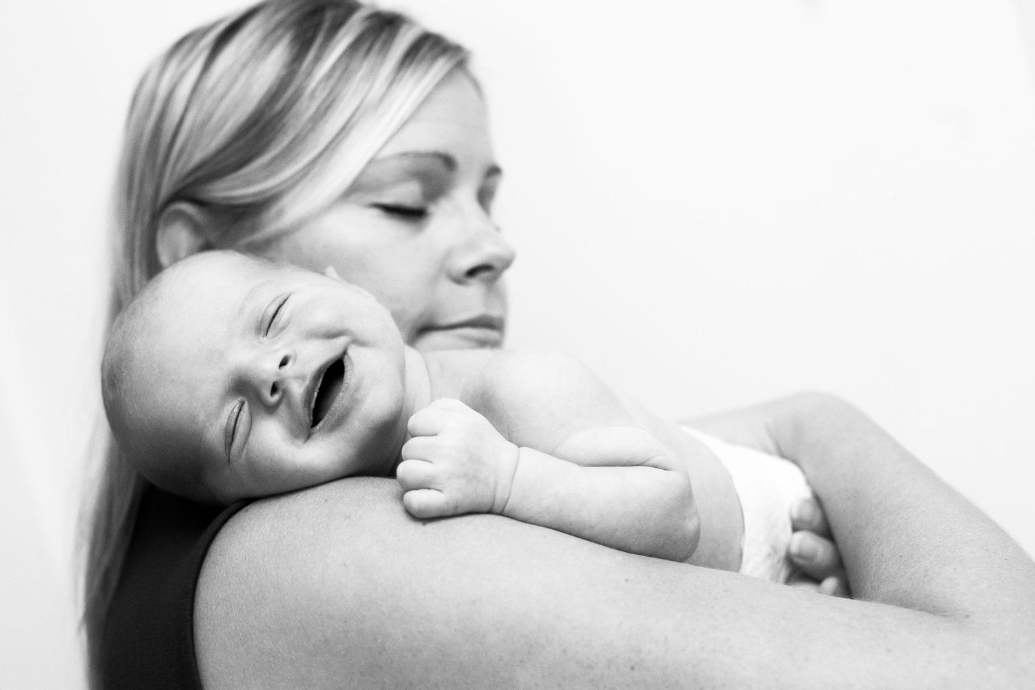 Black and white photo of a smiling newborn baby resting on a blonde mother's arm.