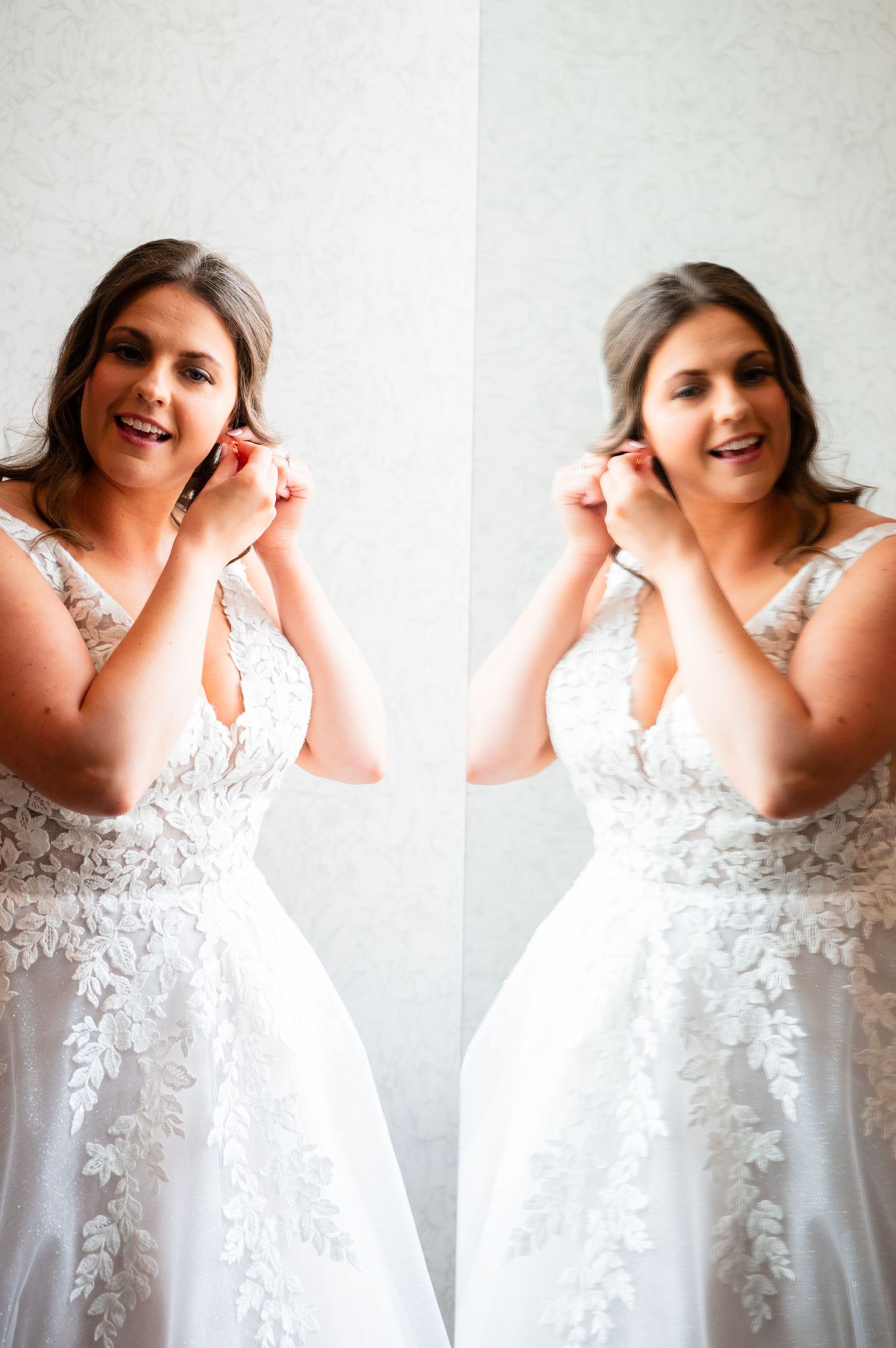 Bride in lace wedding gown putting on earrings reflected in mirror while getting ready.