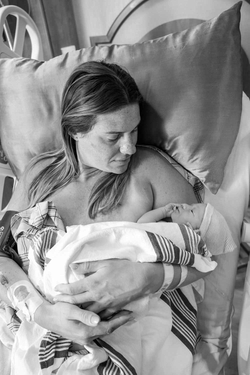 Black and white photo of a new mother cradling her newborn baby in a hospital bed after giving birth.