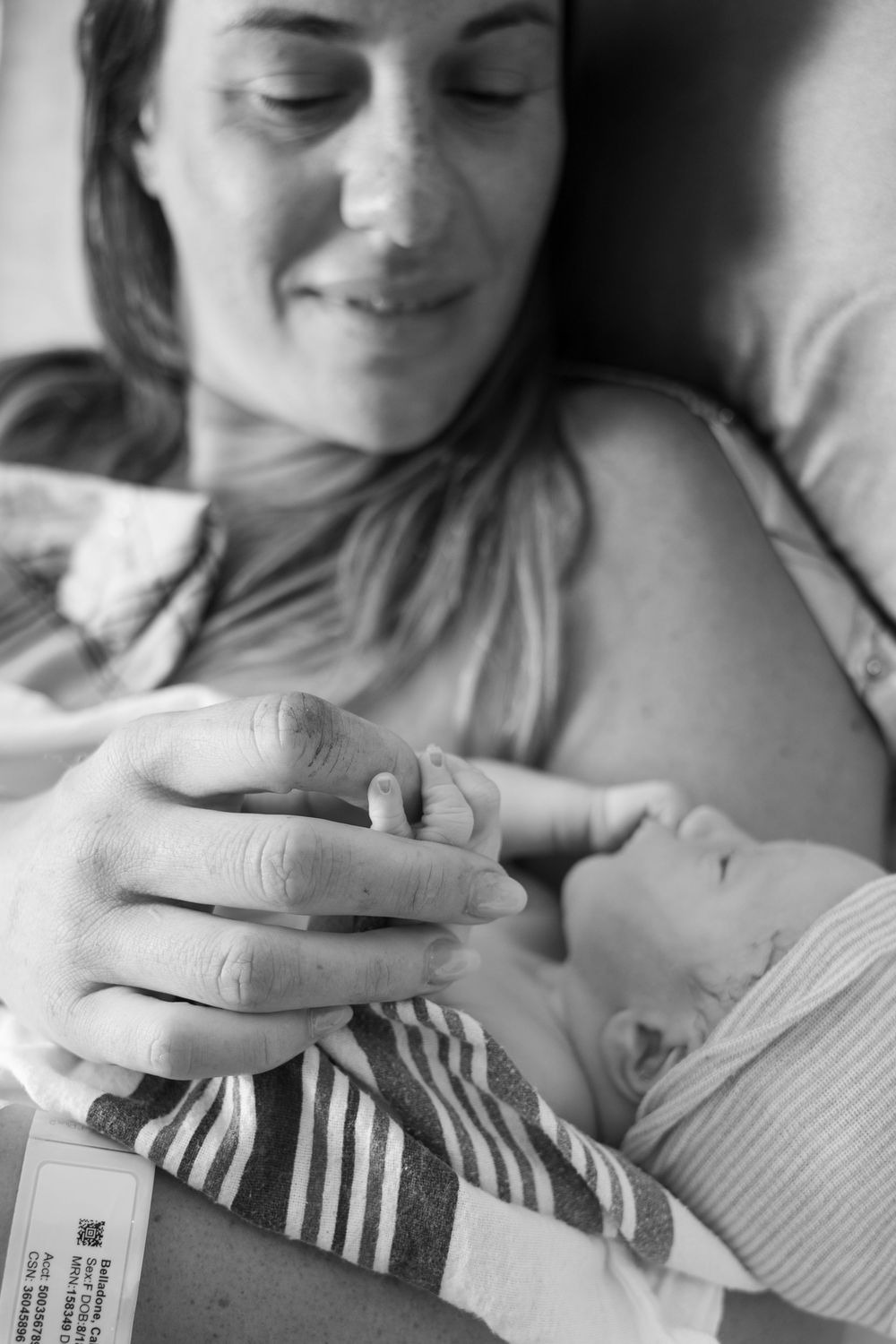 Black and white photo of a smiling new mother holding her newborn baby in a hospital bed.